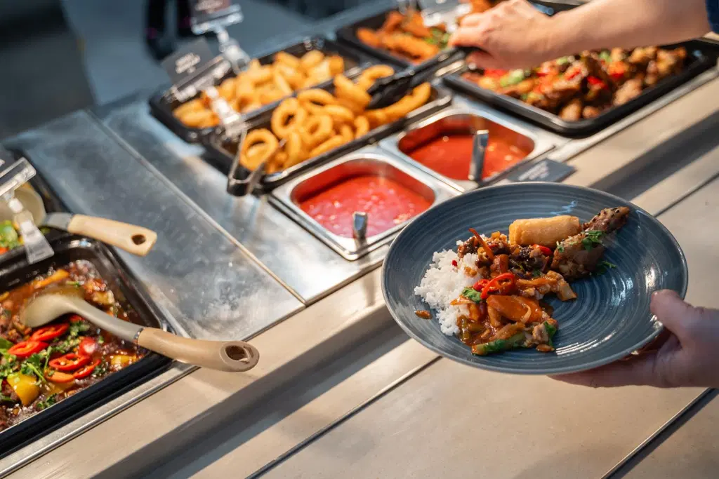 Asiakas poimii noutopöydästä sipulirenkaita lautaselle. Buffetissa tarjolla wokkeja ja muuta aasialaista ruokaa.