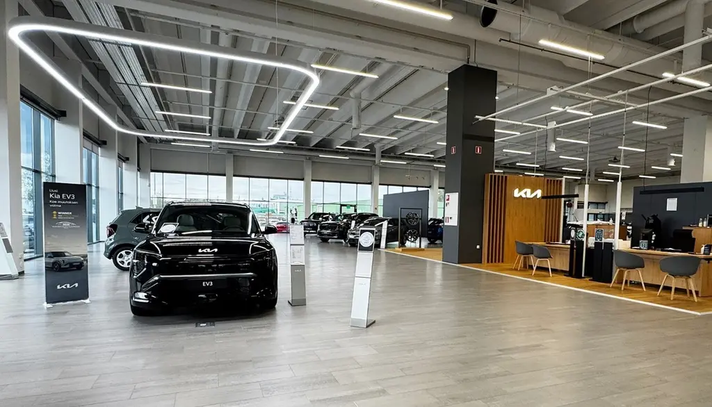 Autoliikkeen valoisa sisätila, jossa autoja ja asiakaspalvelupiste.