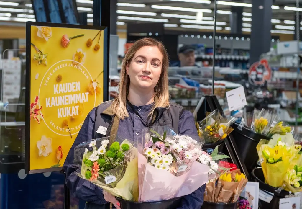 Henkilö kukkakimput sylissään myymäläympäristössä.