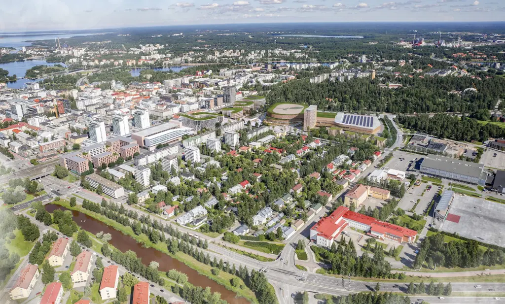  Ilmakuva vihreästä kaupunkialueesta, jossa on sekä korkeita rakennuksia että matalia omakotitaloja, metsää taustalla.