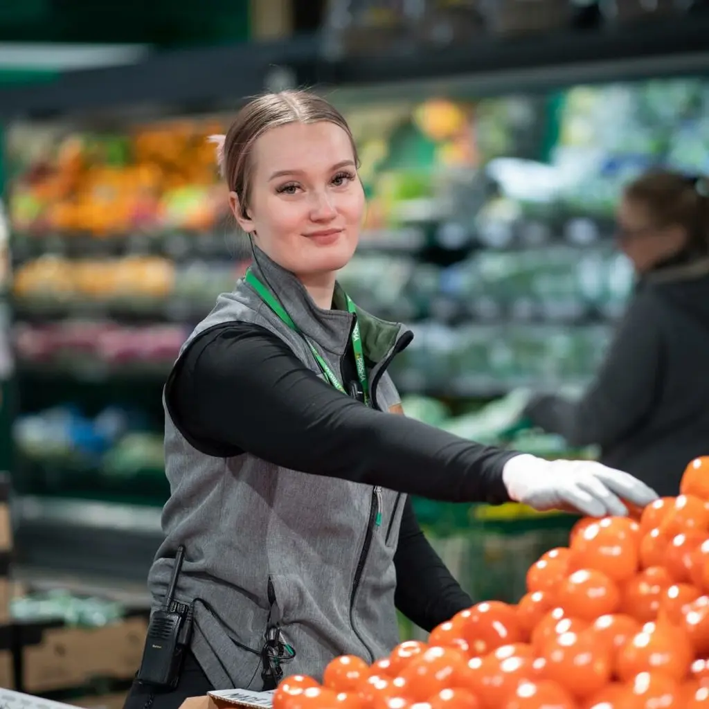 Nuori kaupan työntekijä poimii käteensä tomaattia.
