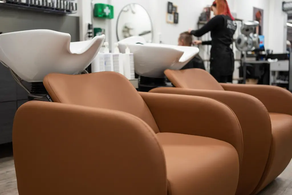 Kampaamotuoleja ja taustalla kampaaja palvelee asiakasta.