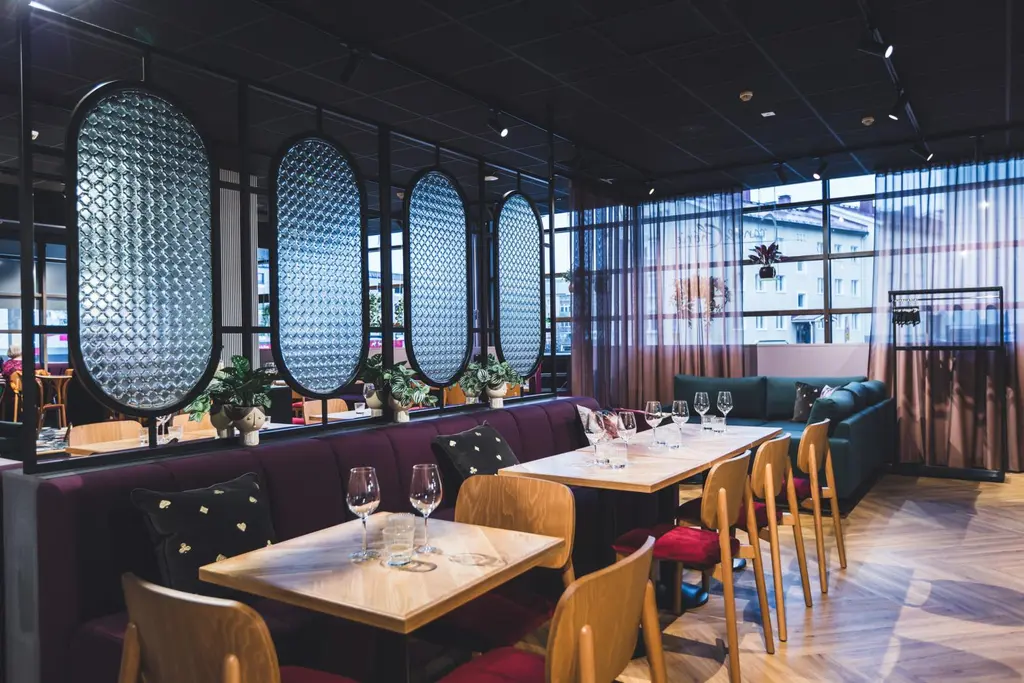 Moderni ravintolasali, jossa on puisia pöytiä, viinilaseja ja kasveja koristeina.