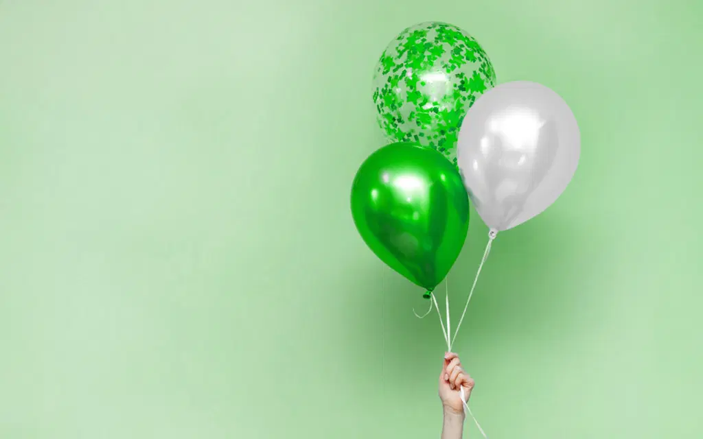Käsi pitelee vihreitä ja valkoisia ilmapalloja vaaleanvihreällä taustalla