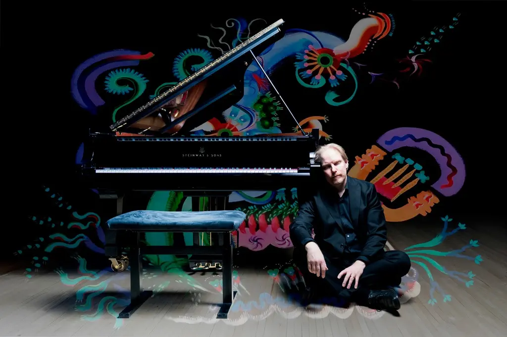 Pianisti Ville Hautakangas istuu lattialla ja uneliaasti nojaa pianoon silmät kiinni