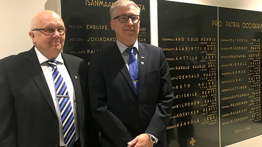 Kaksi miestä seisoo Pro Patria-taulujen edessä hymyillen