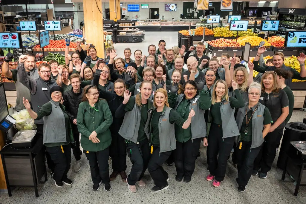 Iso joukko kaupan henkilökuntaa ryhmäkuvassa hedelemä- ja vihannesosastolla.