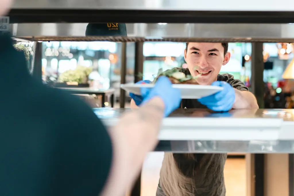 ABC:n työntekijä ottaa keittiöstä vastaan annoslautasen.