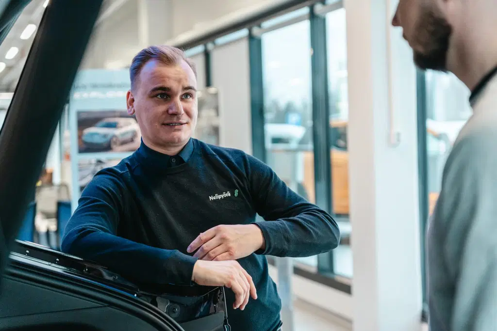 Nelipyörän automyyjä esittelee autoa asiakkaalle.