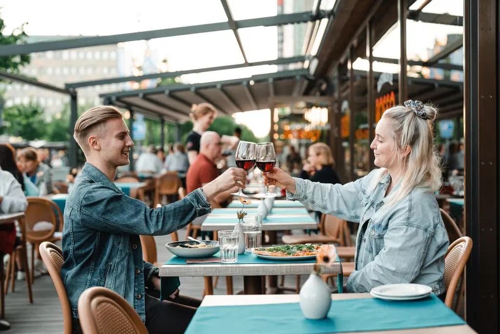 Nuori pariskunta kippistelemässä viinilaseilla Joensuun Rosson terassilla.