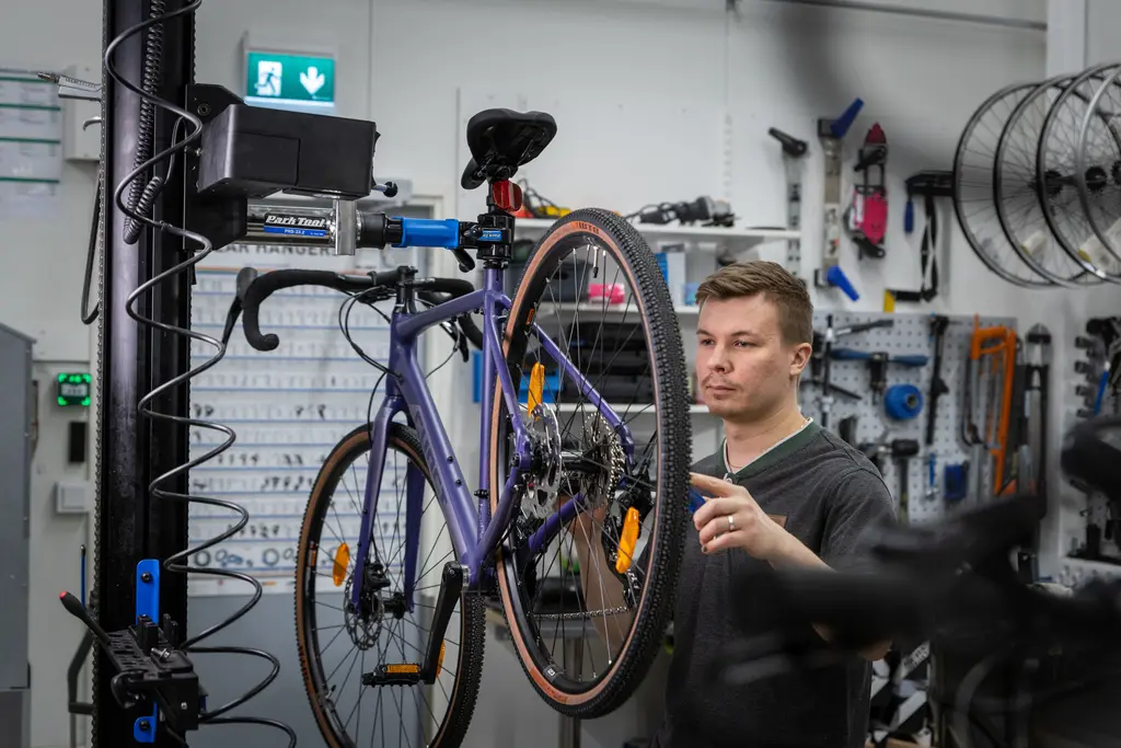 Työntekijä huoltaa violetin pyörän takarengasta.