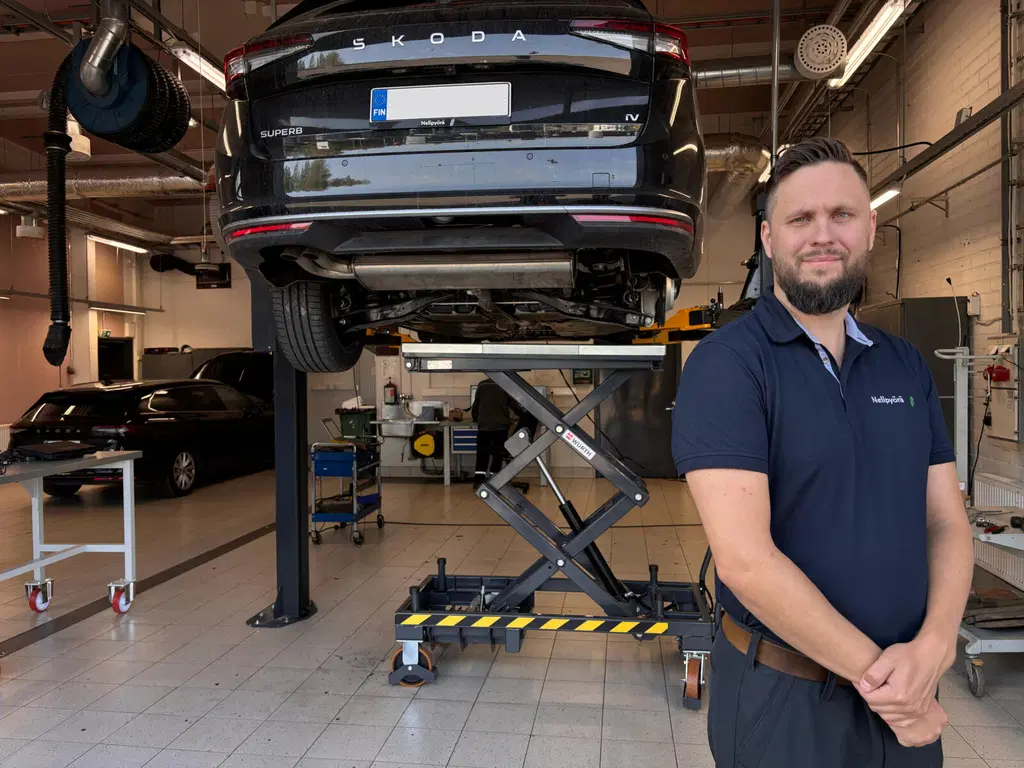 Nelipyörän työntekijä seisoo nostimella olevan auton edessä.