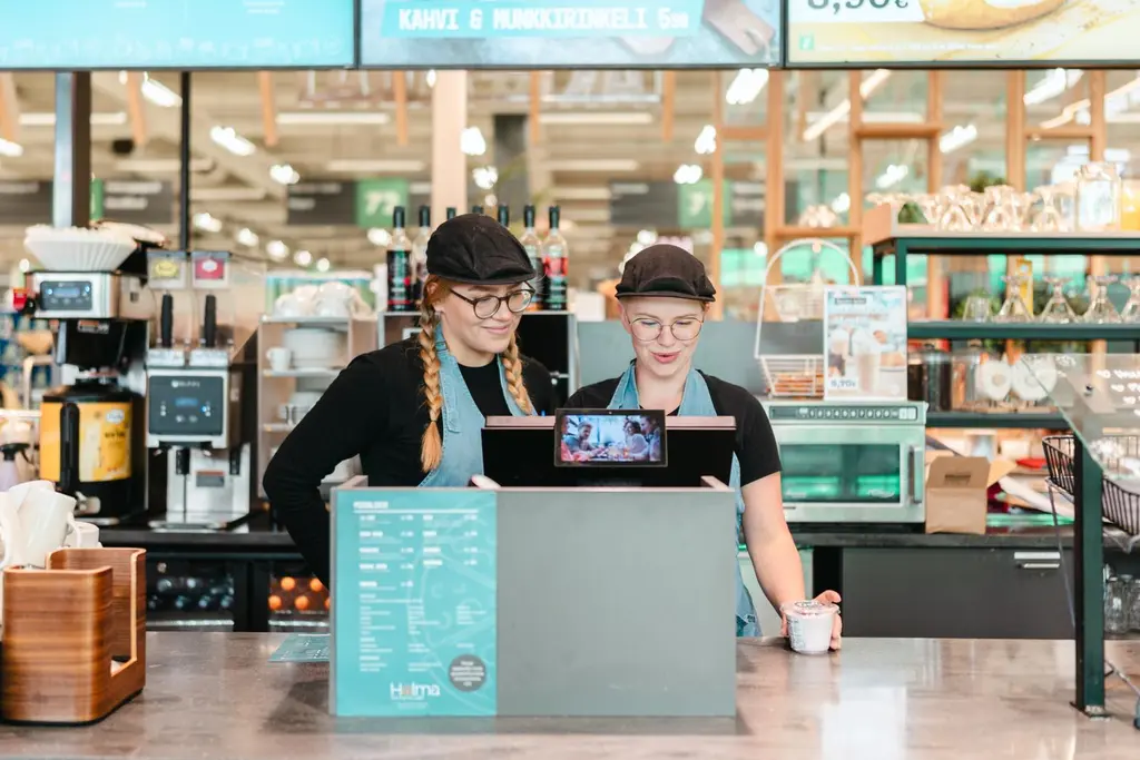 Ravintolamaailman työntekijät seisovat kassan takana ja katsovat jotain päätteeltä.