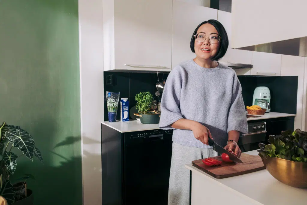 Nainen laittaa pilkkoo tomaattia keittiössä.