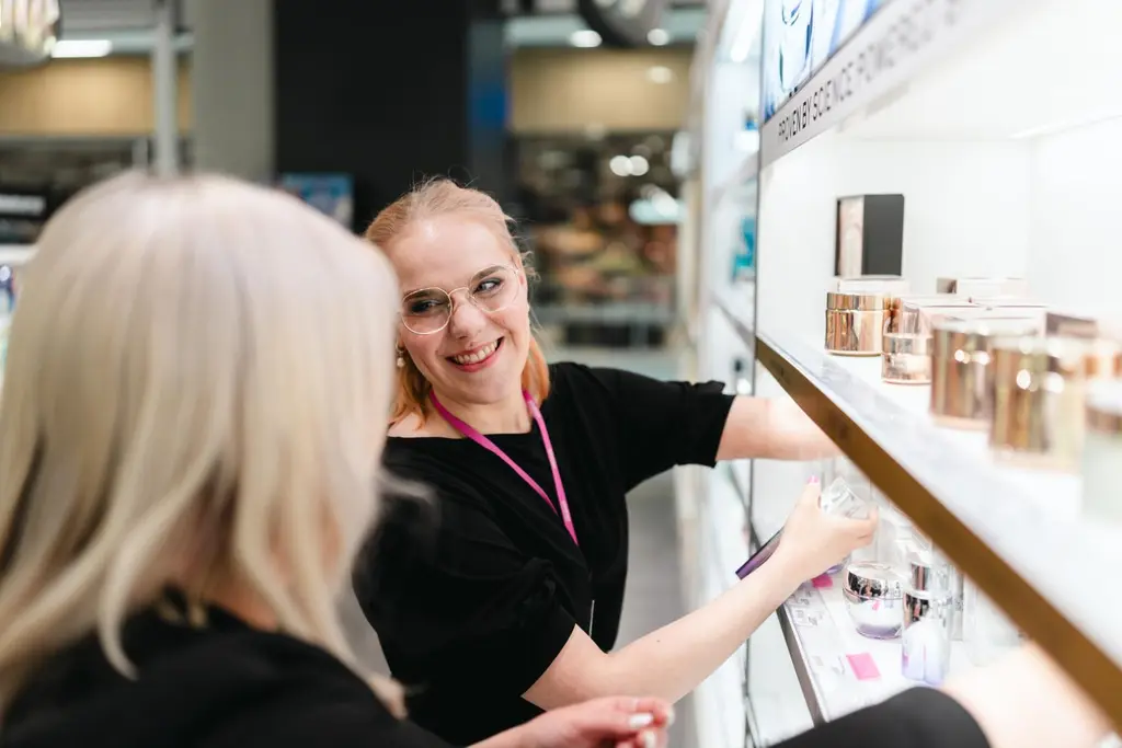 Kaksi Sokos-myyjää hyllyttää tuoksuja. Taaempi työntekijä on kasvot kameraan päin.