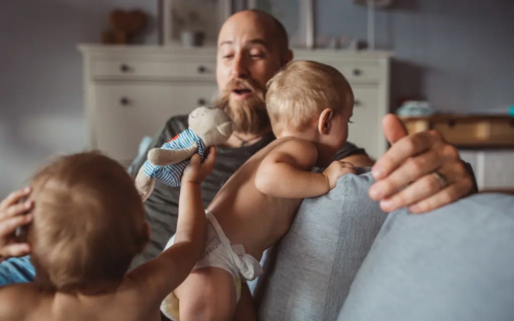 Isä leikkii sohvalla kahden pienen lapsen kanssa.