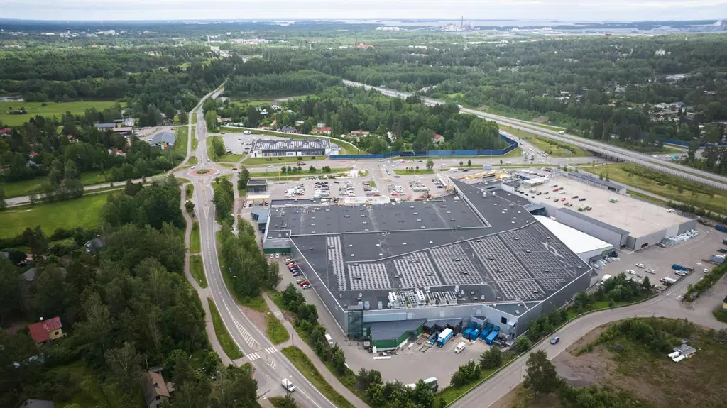 Ilmakuva Kotkan Prismakeskuksesta. Etualalla kauppakeskuskiinteistö ja horisontissa vehreää metsäistä taajamaa ja meri.