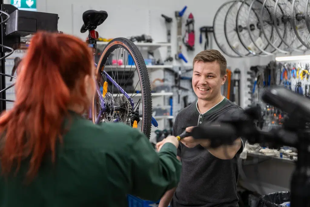Huoltopisteen työntekijä ojentaa hymyillen kollegalleen työkalua.