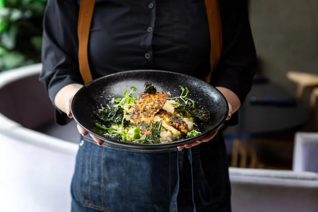 Tarjoilija pitää kädessään ruoka-annosta. Ruokalautanen on kuvan etuosassa.