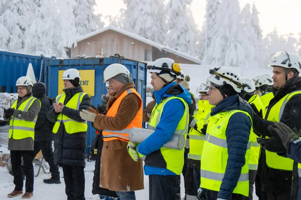 Ryhmä ihmisiä kypärissä ja huomioliiveissä seisoo lumisessa ulkotilassa.