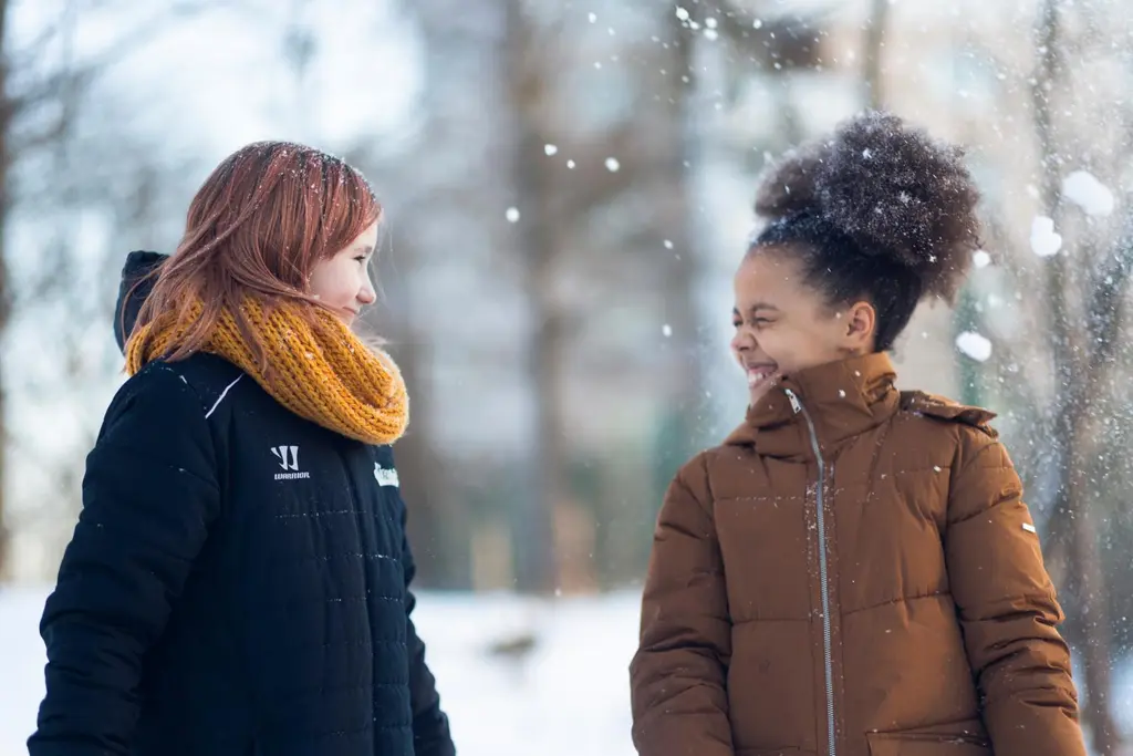 kaksi nuorta, vaalea ja tumma, toppatakit päällä hennossa lumisateessa
