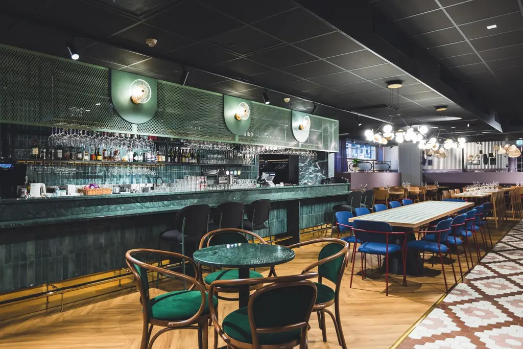 Ravintolan tyylikäs sisustus, jossa on tyhjiä pöytiä ja tuoleja sekä korkea vihreä baaritiski.