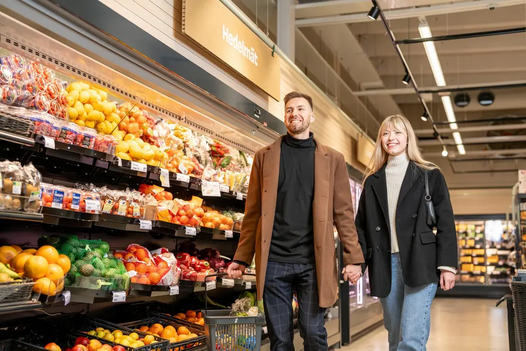 Nainen ja mies kävelevät Sale-myymälän hedelmä- ja vihannesosastolla hymyillen.