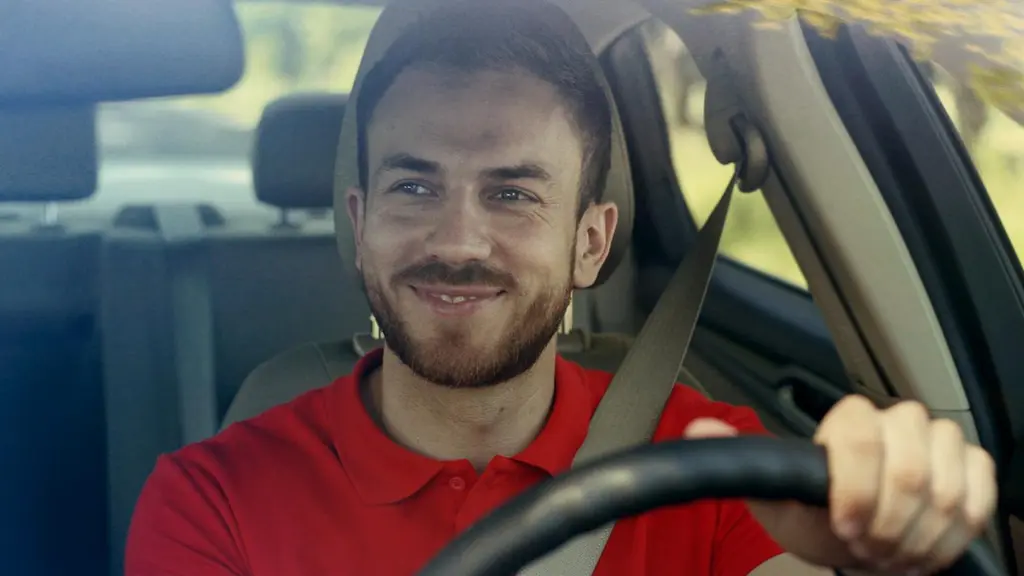 Punapaitainen henkilö ajaa autoa hymyillen.
