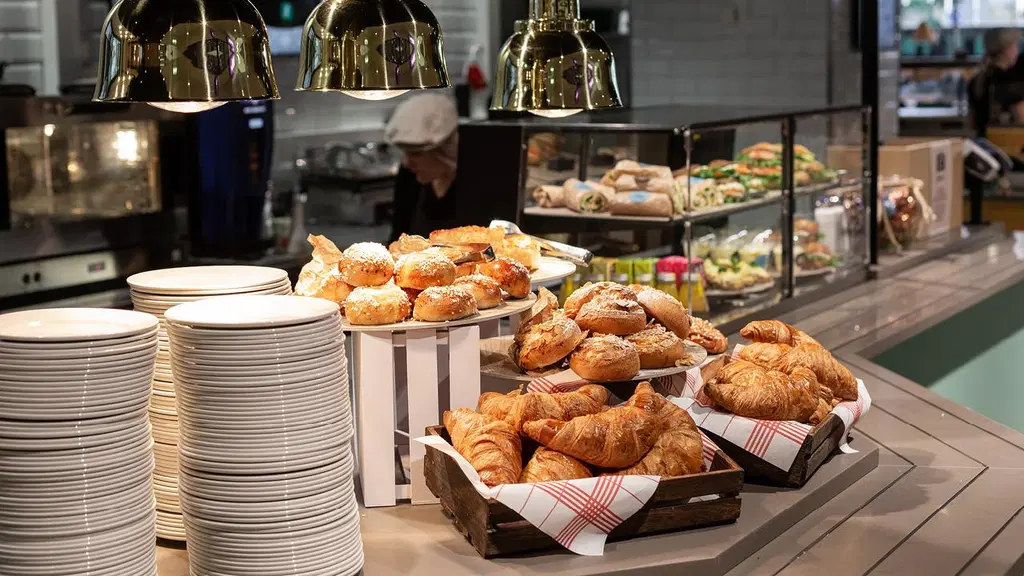Kahvilalinjastolla lautaspino, croisantteja ja pullia koreissa sekä kahvilatuotteita vitriinissä.