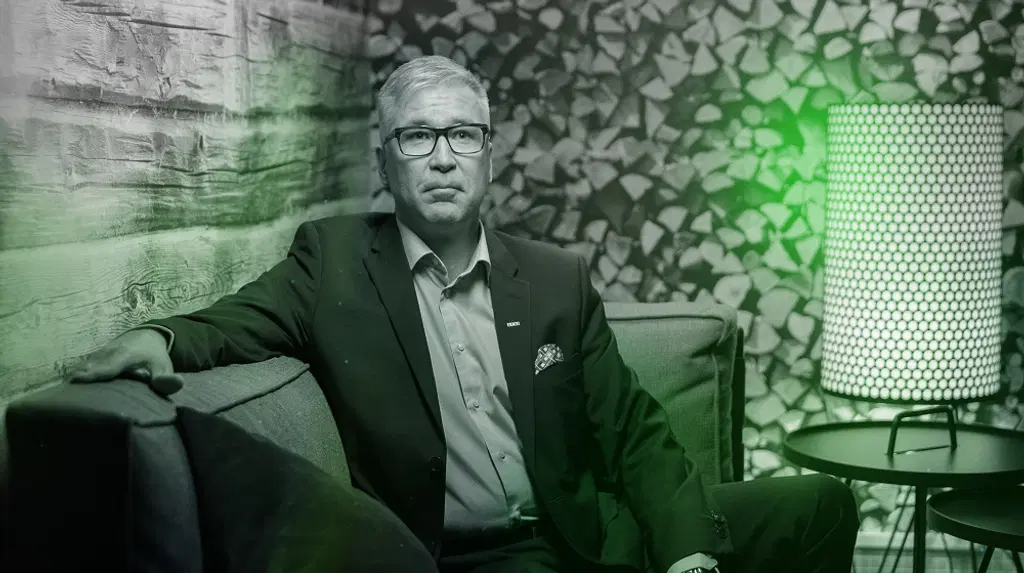 Mies istuu sohvalla ja katsoo kameraan hymyillen