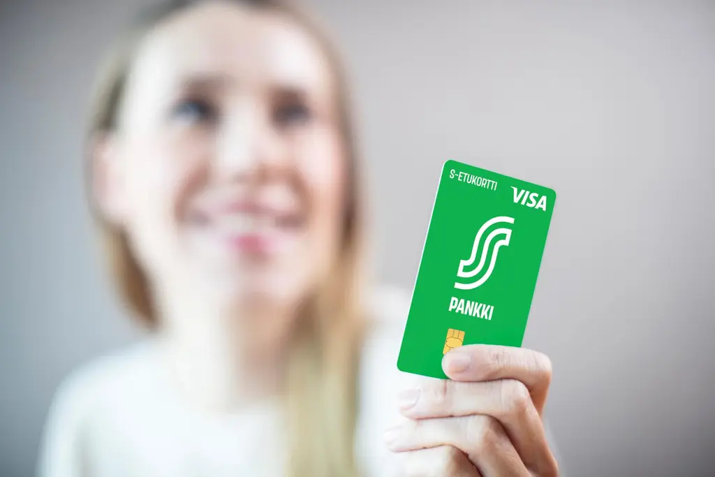 Nainen ojentaa vihreää S-Etukorttia kohti kameraa. Kuvan tausta on epätarkka.