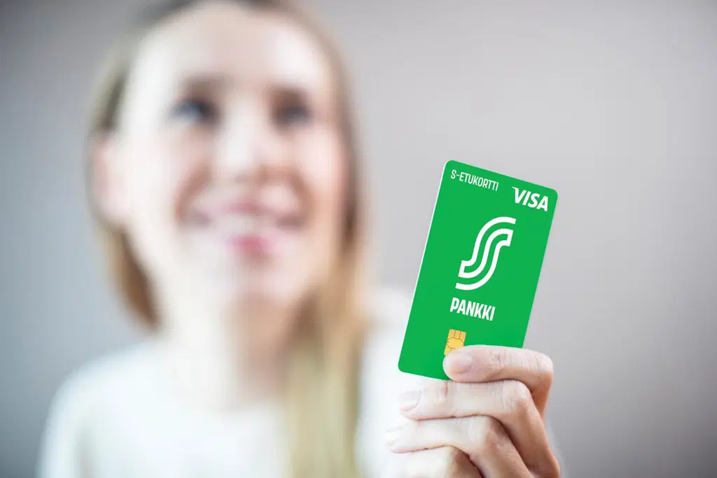 Nainen ojentaa vihreää S-Etukorttia kohti kameraa. Kuvan tausta on epätarkka.