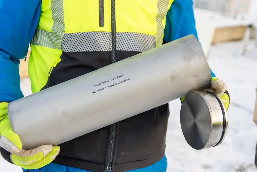 Henkilö pitelee teräksistä säiliötä, jonka päällä on kaiverrettu teksti.