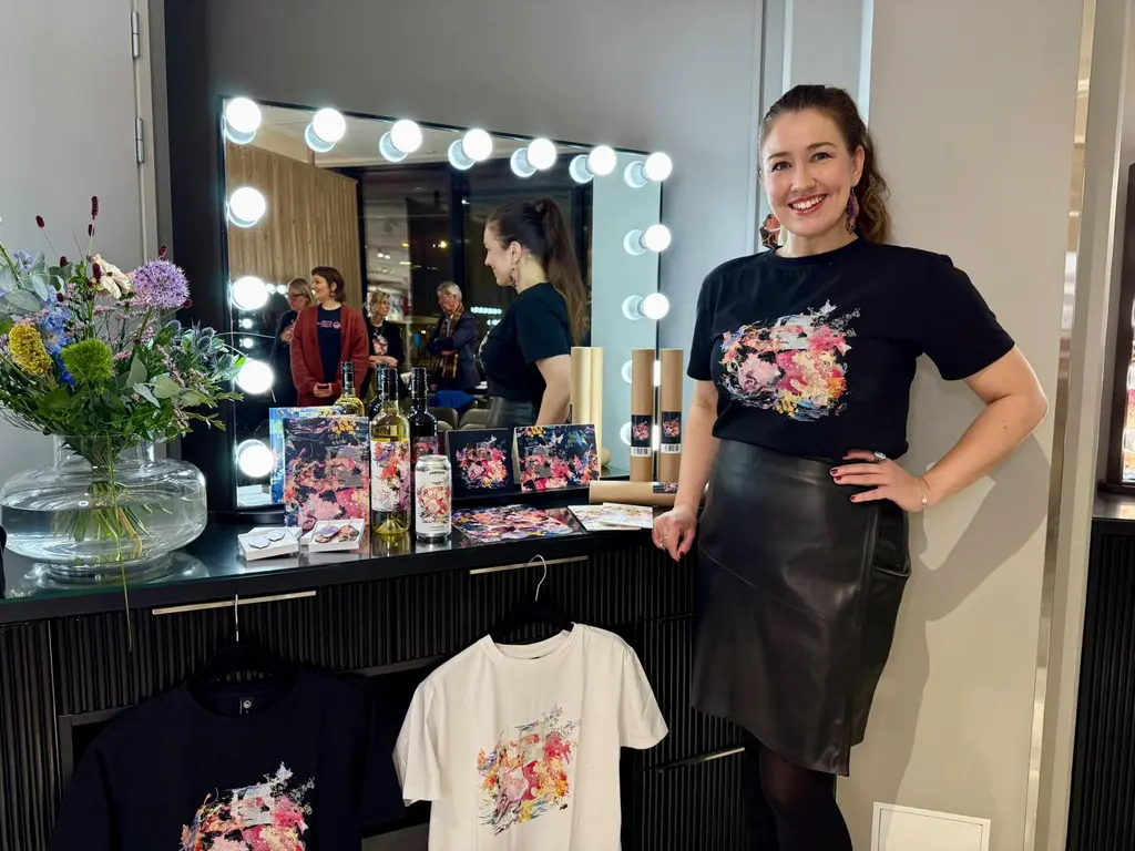 Nainen katsoo hymyillen kameraan. Hänen vieressään pöydällä on erilaisia Mielestäni-tuotteita.