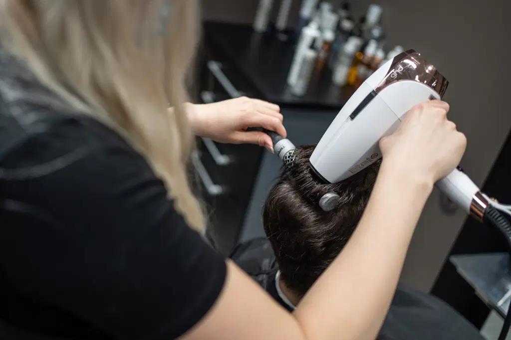 Kampaaja föönaa asiakkaan hiuksia.