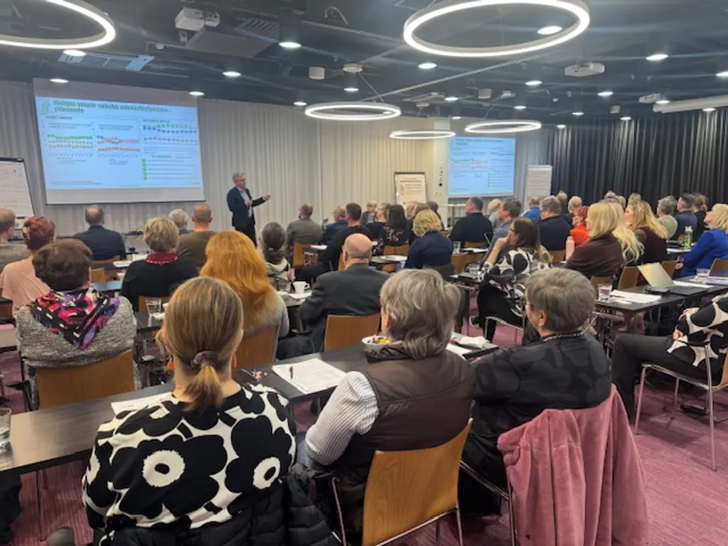 Ihmisiä istumassa kokouksessa. Kuva otettu tilan takaosasta eteenpäin