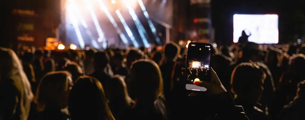 Kuvassa yleisön edustaja kuvaa keikkaa älypuhelimella.