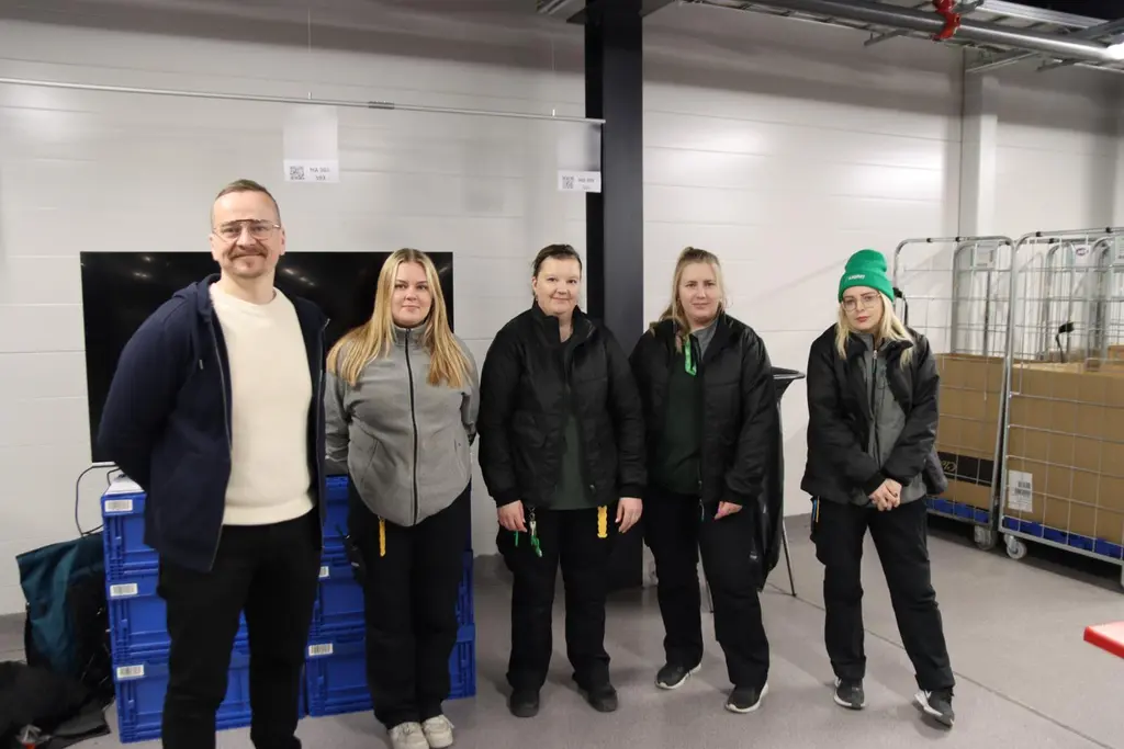 Mies ja neljä naista katsovat kameraan hymyillen