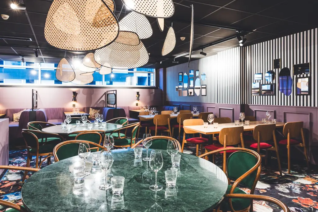 Ravintolasali, jossa on pyöreitä pöytiä ja punaisia sekä puunvärisiä tuoleja. Katossa roikkuvia koristeellisia valaisimia.