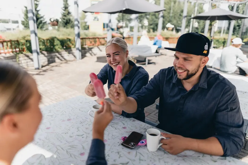 Ryhmä nuoria istuu ulkona pöydän äärellä syömässä mehujäitään.