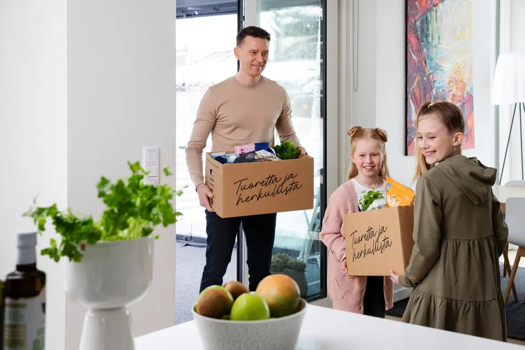 Isä ja kaksi lasta kantavat verkkokaupan ruokaostoksia keittiöön