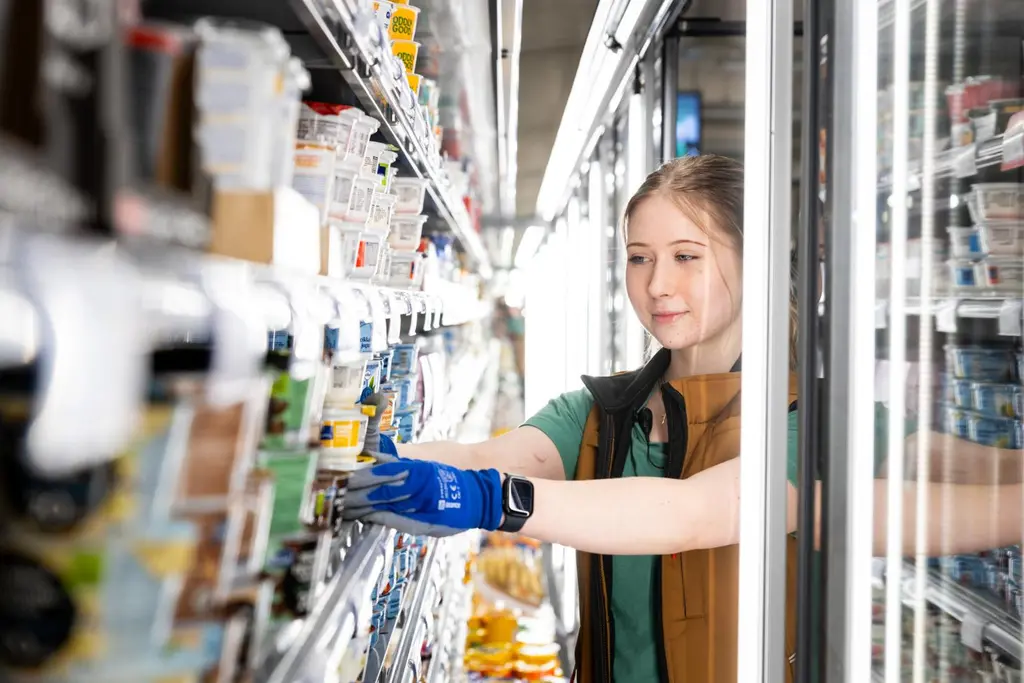 Kaupan työntekijä hyllyttää jogurttipurkkeja.