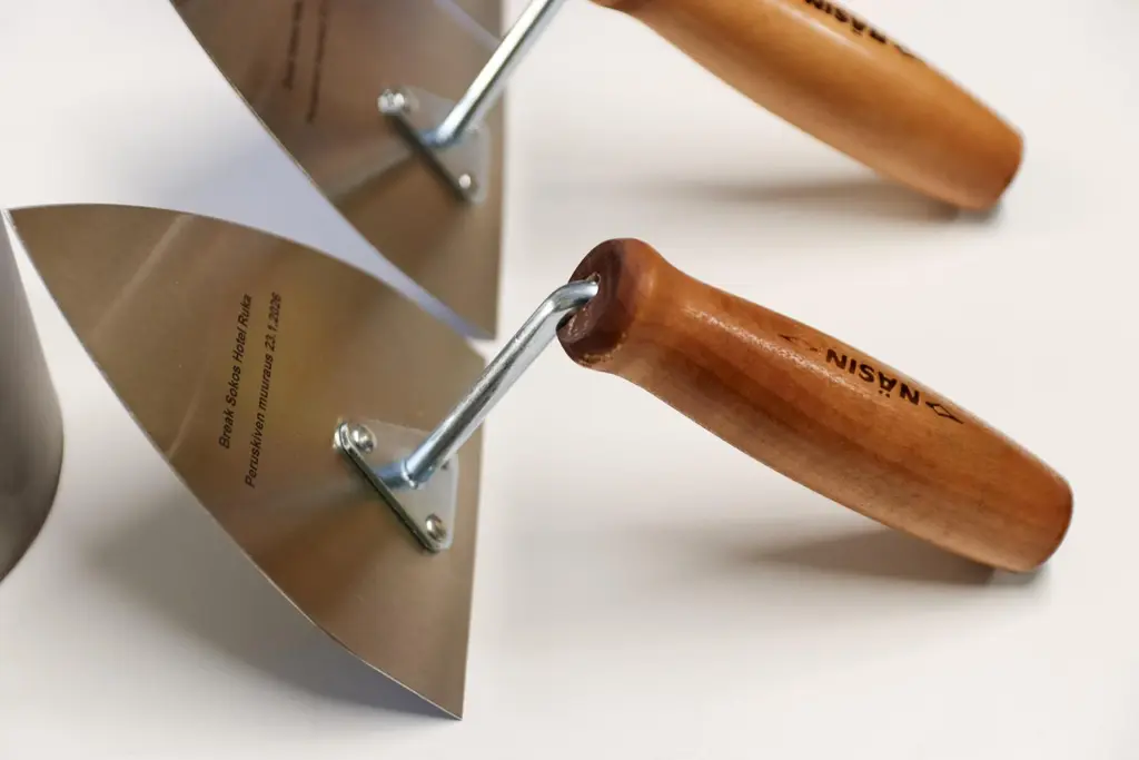 Kolme muurauslastaa puisilla kahvoilla. Lastaosassa teksti "Break Sokos Hotel Ruka - Peruskiven muuraus 23.1.2026"