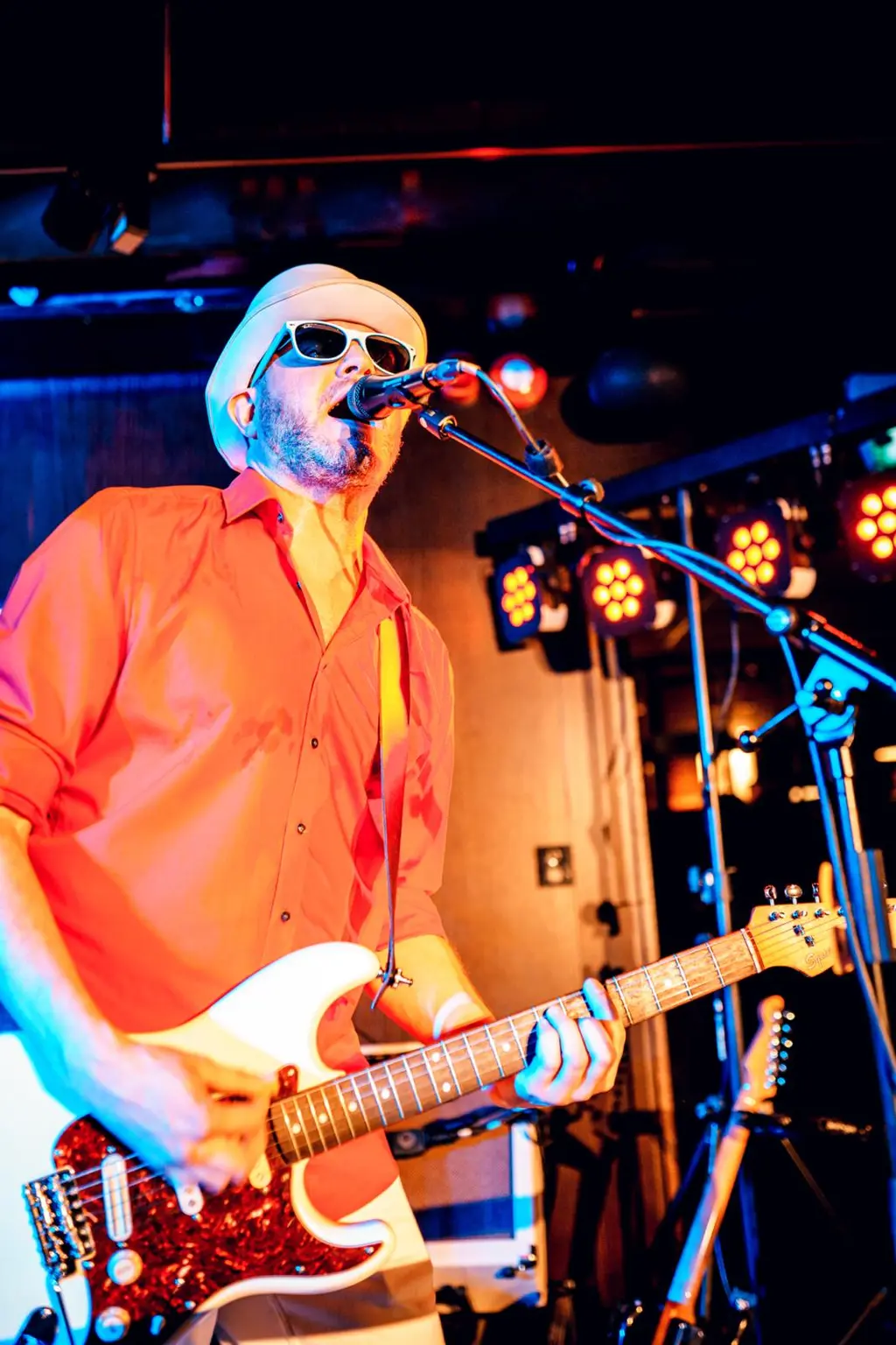 Oranssipukuinen mies esiintyy juhlissa, soittaen kitaraa ja laulaen mikrofoniin.