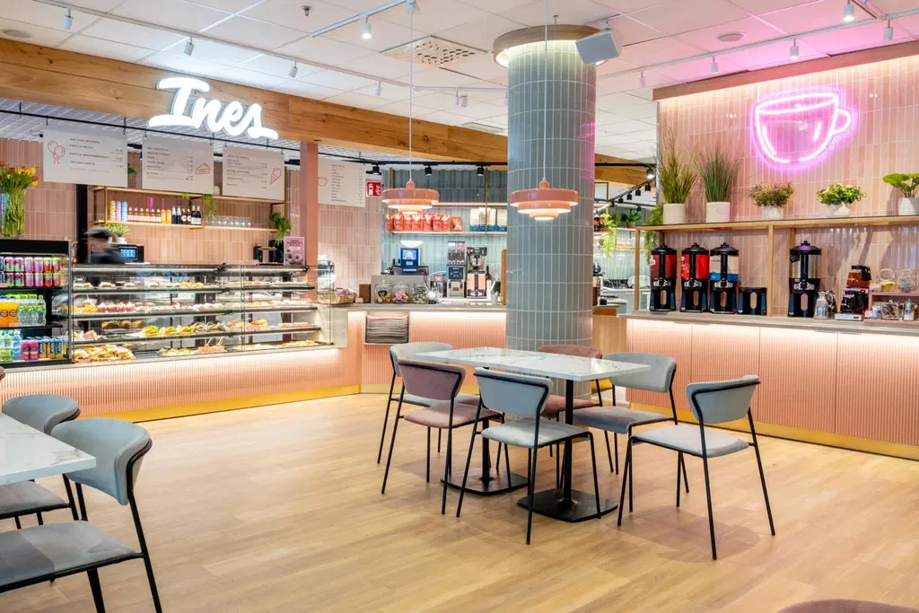 Lahden Sokoksen ravintolamaailmassa sijaitseva Ines café on sisustettu valoisasti hempeän vaaleanpunaisin ja vihrein sävyin. Seinällä on suuri pinkki neonvalokyltti, joka esittää kahvikuppia.