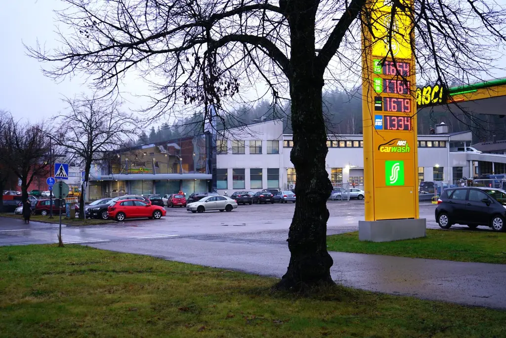 Parkkipaikka ja harmaa liikerakennus sateisena syyspäivänä. Etualalla ABC:n keltainen pyloni.