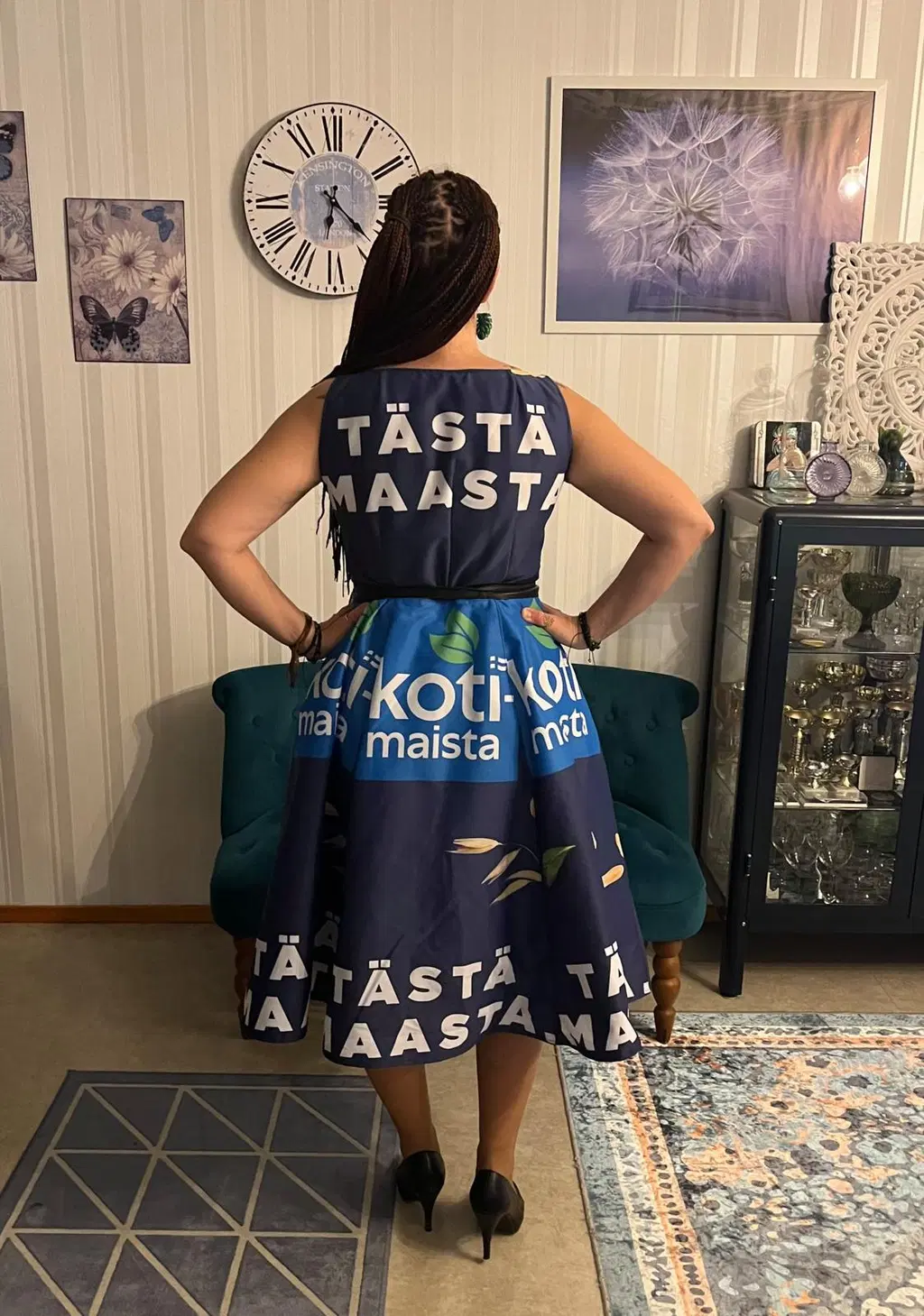 Nainen seisoo selin kameraan. Hänellä on yllään mekko, jonka kuosina on S-ryhmän Kotimaista-tuotesarja.