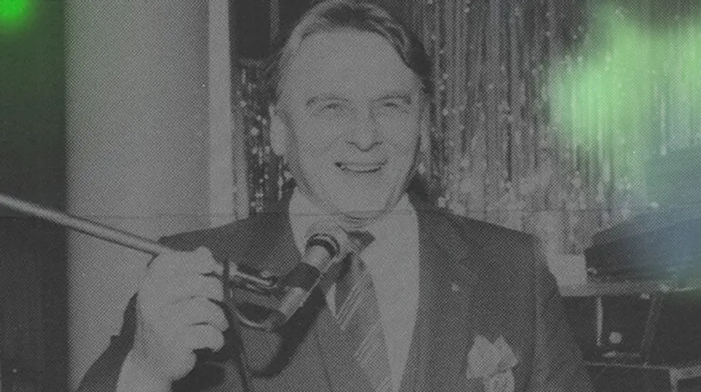 Mies hymyilee puhuessaan mikrofoniin