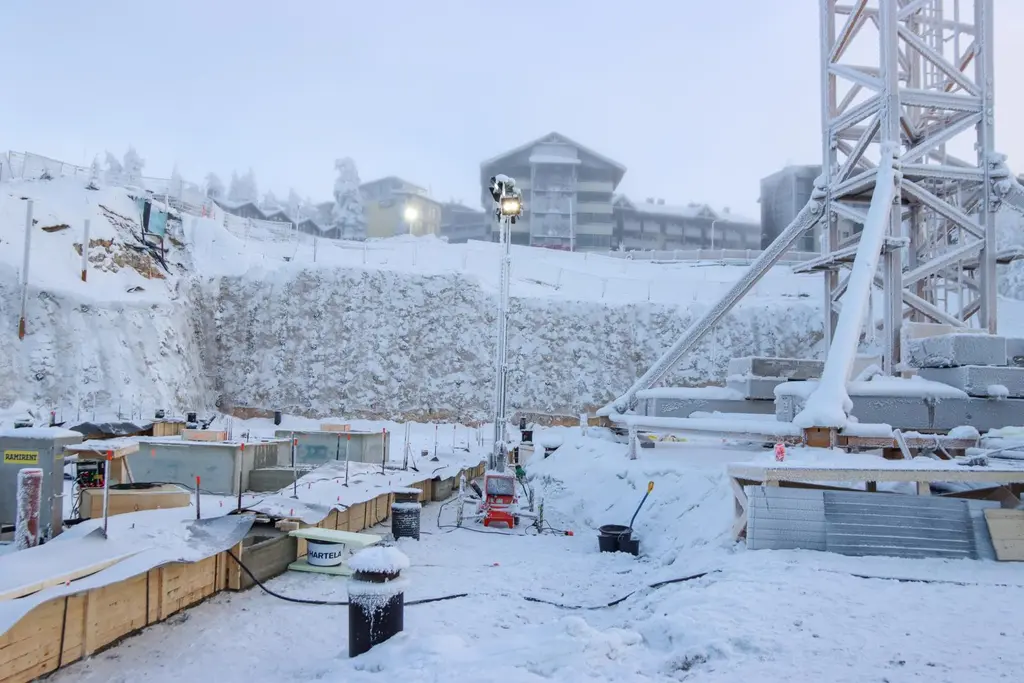 Talvinen rakennustyömaa, jossa paljon lunta. Taustalla taloja ja suuri nosturi.