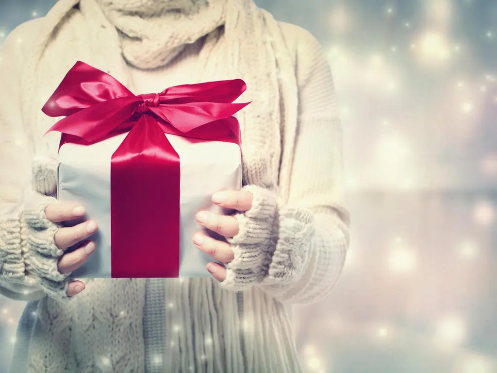 Nainen valkoisessa neuleessa pitelee lahjapakettia ympärillään tähtiloistetta